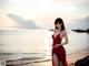 A woman in a red dress standing on a beach.