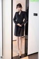 A woman in a black trench coat standing in front of a mirror.