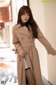 A woman in a beige trench coat is posing for a picture.