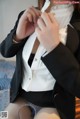 A woman in a black suit and white shirt is putting on her panties.