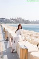 A woman in a white dress sitting on a wall by the water.