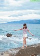 A woman standing on a rock by the ocean with her arms outstretched.