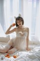 A woman in a white lingerie sitting on a bed holding an orange.