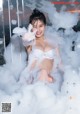 A woman in a white bra sitting in a bathtub covered in foam.