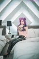 A woman with purple hair sitting on a bed.