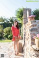 A woman in a red polka dot dress standing in front of a stone wall.