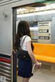 A woman in a white shirt and blue skirt standing on a subway train.