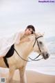 A woman in a white dress riding a white horse on the beach.