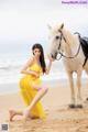 A woman in a yellow dress standing next to a white horse.