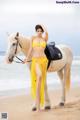 A woman in a yellow bikini standing next to a white horse.