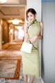 A woman in a green dress leaning against a wall.