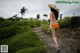 A woman in an orange bikini and a straw hat walking down a path.