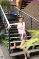 A woman in a pink top and colorful shorts posing on some stairs.