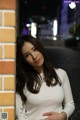 A woman leaning against a brick wall at night.