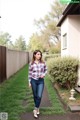 A woman in a plaid shirt and jeans standing in a yard.