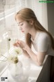 A woman sitting at a window sill with a vase of flowers.