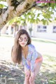 A woman in a bikini and sunglasses posing under a tree.