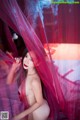 A naked woman is posing in front of a red curtain.