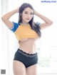 A woman in a yellow shirt and black panties posing for a picture.