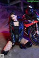 A woman in a leather jacket and fishnet stockings posing next to a motorcycle.