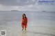 A woman in a red dress standing in the ocean.