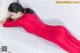 A woman in a red bodysuit laying on a white couch.