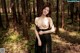 A woman in a black dress standing in the woods.