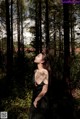 A woman in a black dress standing in the woods.