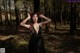 A woman in a black dress standing in the woods.