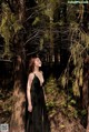 A woman in a black dress standing in the woods.