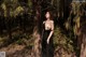 A woman in a black dress standing in the woods.