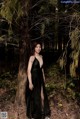 A woman in a black dress standing in the woods.