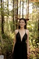 A woman in a black dress standing in the woods.