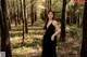 A woman in a black dress standing in the woods.