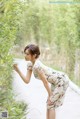 A woman in a white dress leaning against a bamboo tree.