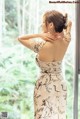 A woman in a white dress standing by a window.