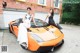 Two women sitting on top of an orange sports car.