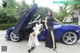 A couple of women standing next to a blue sports car.