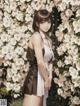 A woman standing in front of a wall of white flowers.