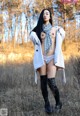 A woman in a white coat and scarf standing in a field.