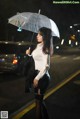 A woman in a white shirt and black skirt holding an umbrella.