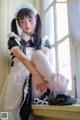 A woman in a maid outfit sitting on a window sill.